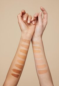 Två armar visar stiftelseprover i olika nyanser. Vänster arm: djup bruna till ljusbruna. Höger arm: ljus beige till blek. Släta texturer.