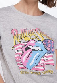 Camiseta gris con el colorido logo de la lengua de los Rolling Stones, que presenta rayas rosas, azules y blancas, y el texto amarillo "Steel Wheels Tour 89".