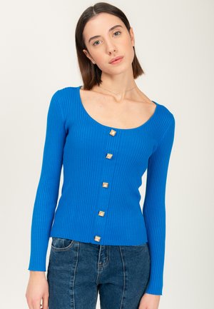 Blauw geribbelde langwerpige top met een wijde ronde halslijn en vier vierkante gouden knopen aan de voorkant. Zachte textuur, aansluitende pasvorm.