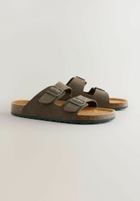 Sandales ajustables marron avec un dessus texturé, semelle intérieure en liège et semelle en caoutchouc. Présente deux boucles métalliques et un design plat.