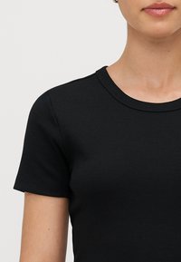 Fekete bordázott rövid ujjú póló kerek nyakkivágással, sima textúrával és testhez álló kialakítással, amely kiemeli a nyak és a váll területét.