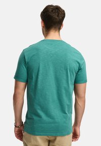 T-shirt a maniche corte di colore teal realizzato in tessuto leggero. Presenta un collo rotondo e una superficie liscia, con dettagli di cucitura visibili.
