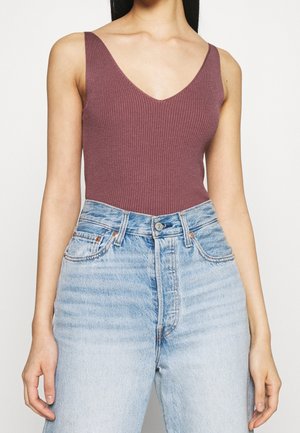 Débardeur ajusté mauve côtelé à fines bretelles, porté rentré dans un jean en denim bleu clair taille haute sur une personne debout.