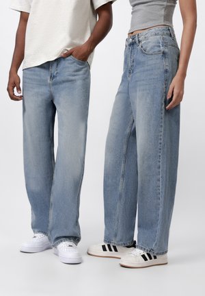 Light blue denim jeans with a wide, loose fit, featuring classic five-pocket design and subtle fading. Paired with white and black sneakers.