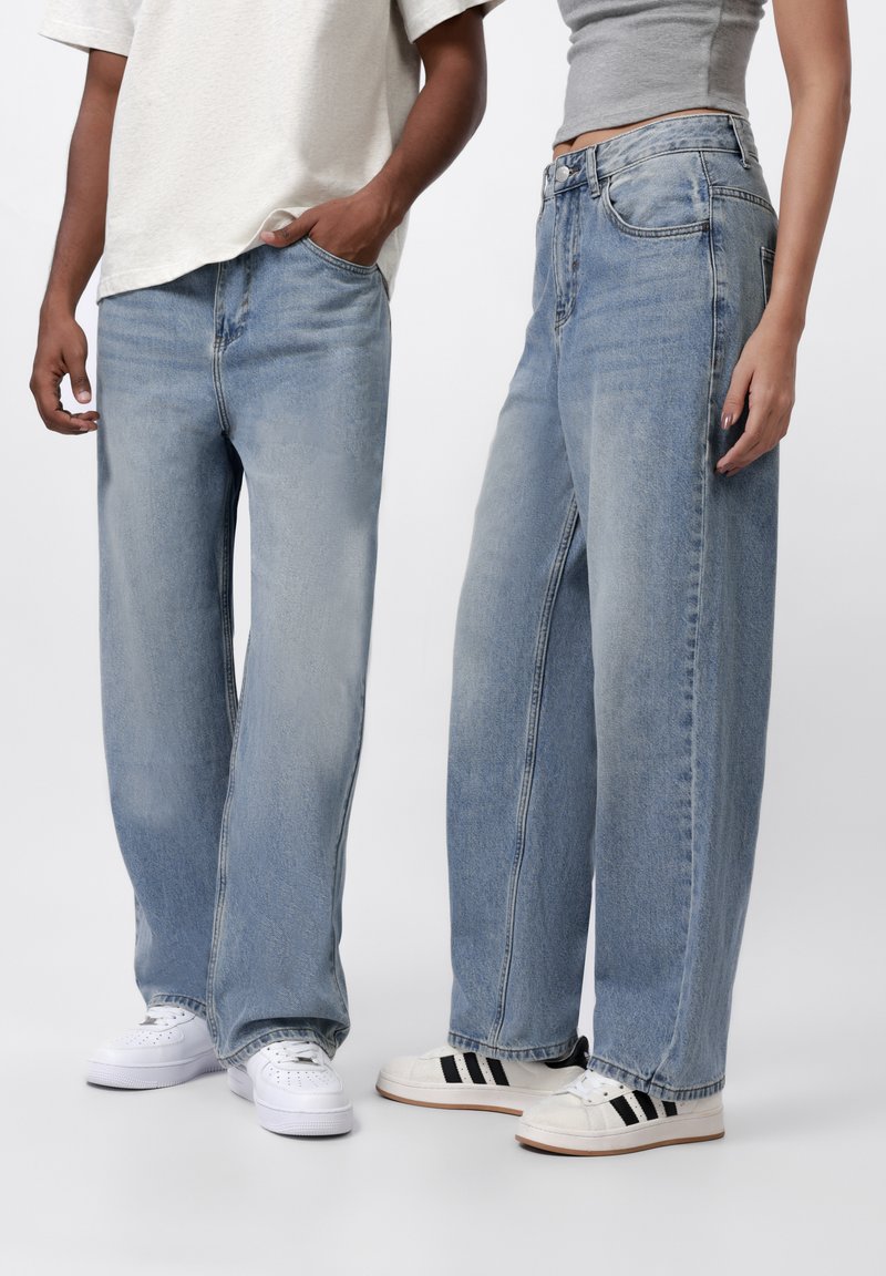 Lys blå denimjeans med vid og løs passform, med klassisk fem-lomme-design og subtil falming. Kombinert med hvite og sorte joggesko.