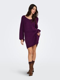 Oversized purple sweater with a wide neckline and long sleeves, made from a textured knit fabric, worn over a short hemline.