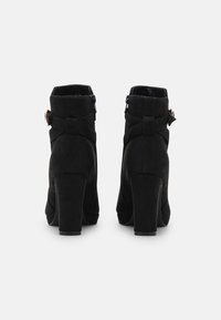 Schwarze Wildleder-Stiefeletten mit einem robusten Absatz, seitlichem Reißverschluss und dekorativen Riemen mit einer runden goldenen Schnalle. Glatte Textur, abgerundete Zehe.