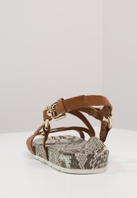 Brown leather sandals featuring a textured snake print platform and gold hardware accents. Strap design with buckle closure at the ankle.
