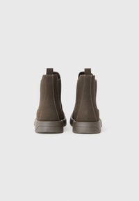Botines de tela marrón con paneles laterales elásticos, lengüetas de tirón y suelas de goma. El detalle de costura a lo largo de las costuras realza el diseño.