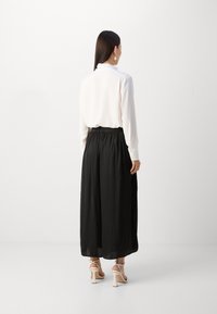 Vit blus med lång ärm i kombination med en svart, svängande kjol. Kjolen har resårmidja och är ankel-lång, tillverkad av ett lätt material.