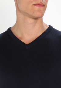 Pull tricoté bleu marine avec un col en V. Présente un col côtelé et une texture lisse, idéal pour une tenue décontractée.