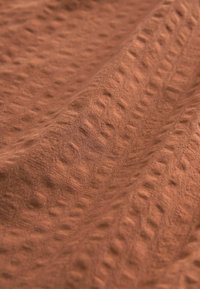Tessuto texturizzato in una calda tonalità di marrone terra, caratterizzato da un motivo a puntini in rilievo e una superficie morbida al tatto. Effetto di drappeggio liscio.