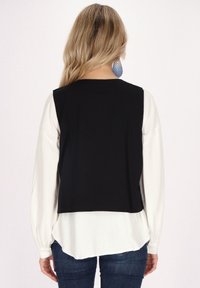 Schwarzes ärmelloses Top über einer weißen Bluse mit langen Ärmeln; hat einen runden Ausschnitt, klare Linien und eine glatte Textur.