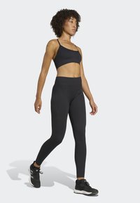 Tenue de sport noire comprenant un soutien-gorge de sport ajusté avec des fines bretelles et des leggings taille haute à texture côtelée, associés à des baskets noires.