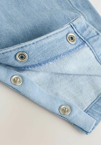 Gros plan sur un tissu en denim présentant des boutons-pression argentés et un bord replié, mettant en valeur la texture et la variation de couleur du denim bleu clair.