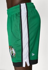 Calções de basquetebol verdes feitos de tecido de malha, com um design riscado em preto e branco, e um logótipo bordado dos Boston Celtics.