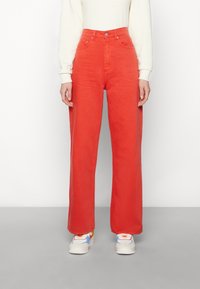 Hochtaillierte, weit geschnittene Jeans aus leuchtend rotem Denim. Mit Knopfverschluss, Fünf-Taschen-Design und einer weichen Textur. Kombiniert mit bunten Sneakern.