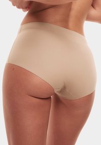 Beige sömlösa tanga-short med medelhög midja, tillverkade av ett glatt, stretchy tyg, utan synliga sömmar för en strömlinjeformad look.