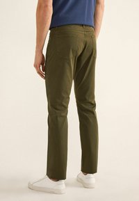 Pantalones de algodón verde oliva con corte recto, que cuentan con bolsillos traseros y cinturilla ajustada, combinados con zapatillas blancas.