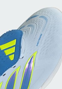 Gros plan sur une chaussure de sport blanche avec une languette bleue, des accents jaunes et violets, et le texte "NANOSTRIKEPRO" sur le côté supérieur.