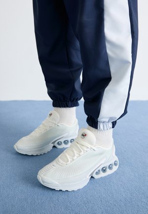 Weiße Netzsneaker mit strukturierter Oberfläche, die klare Blasenakzente in der Sohle und ein kleines Logo auf der Zunge aufweisen. Tragen sie mit navy blauen Jogginghosen.