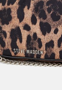 Kabelka z látky s leopardím vzorem, se stříbrným řetězovým popruhem a kovovým logem "Steve Madden" na přední straně. Hladký povrch a kompaktní tvar.