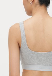Šedý žebrovaný bralet s širokými ramínky a bezšvovým designem. Disponuje měkkým elastickým páskem s embosovaným nápisem "Organic Basics". Hladká textura.