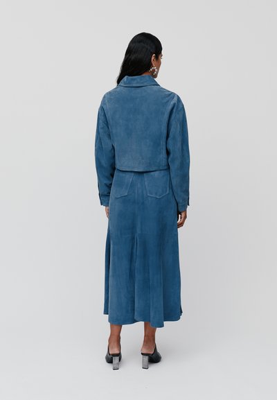Cappotto in suede blu con un design corto, maniche lunghe e chiusura con bottoni. Presenta una gonna di lunghezza intermedia e un taglio dritto.