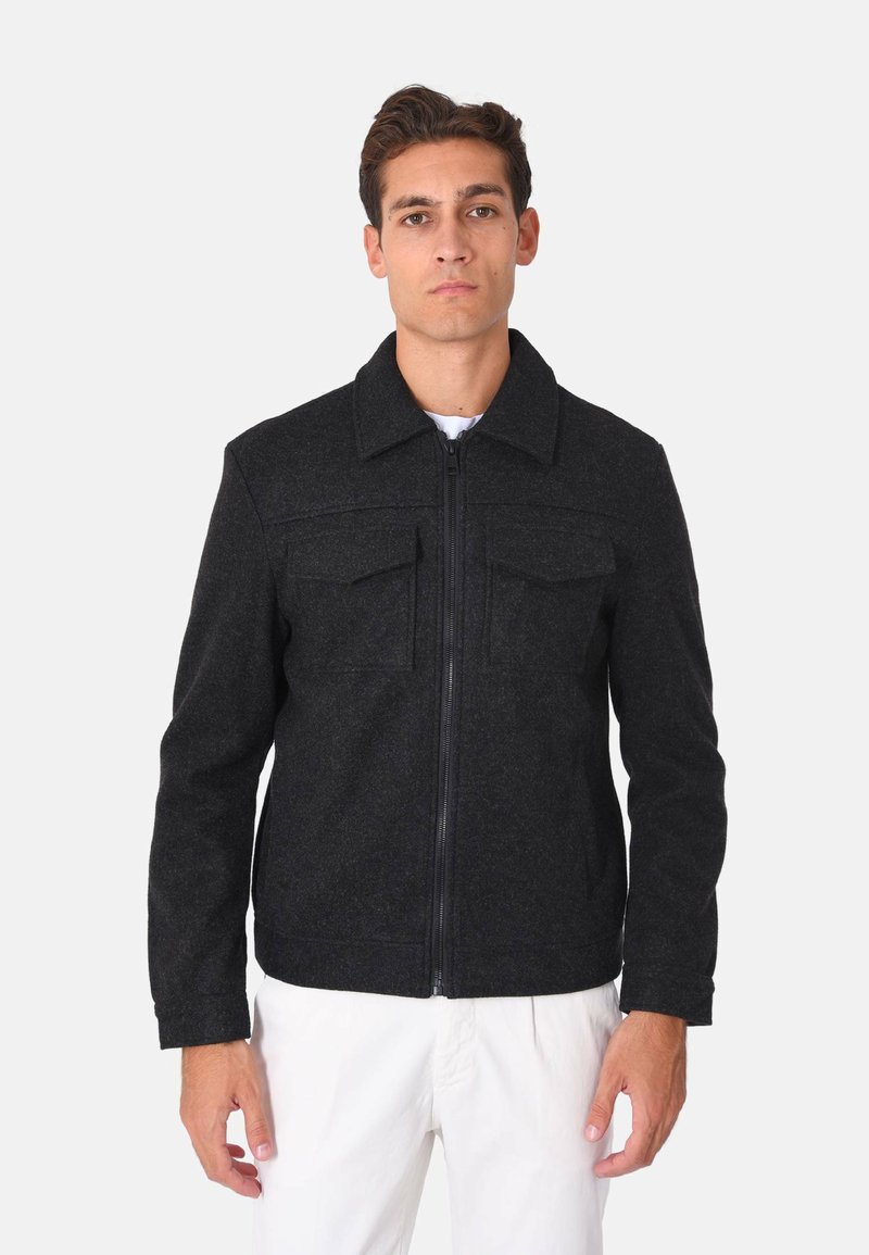 Giacca nera in misto lana con colletto, chiusura frontale a zip e due tasche sul petto. Presenta una vestibilità sartoriale e una texture liscia.