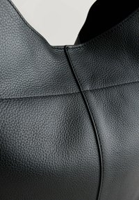 Materiale in pelle nera con una texture granulosa, con cuciture visibili e un design curvo. Non sono presenti hardware o accenti aggiuntivi.