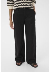 Pantaloni larghi neri, leggeri, con un design pulito e tasche laterali, abbinati a sandali aperti e testurizzati.
