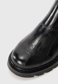 Bottines en cuir noir avec une finition texturée, un bout arrondi et une semelle en caoutchouc robuste avec des crampons bien définis.