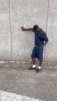 Conjunto de denim featuring uma camisa de mangas curtas com costura laranja e calções até ao joelho combinando, emparelhados com sapatos pretos e meias brancas.