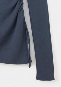 Gros plan d'un haut en maille bleu foncé à manches longues avec des liens latéraux et un motif de tissu texturé.