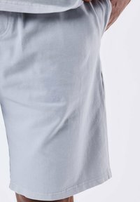 Bermudas de algodón gris claro con una textura suave, bolsillos laterales y un corte recto. El dobladillo y las costuras están terminados de manera limpia.