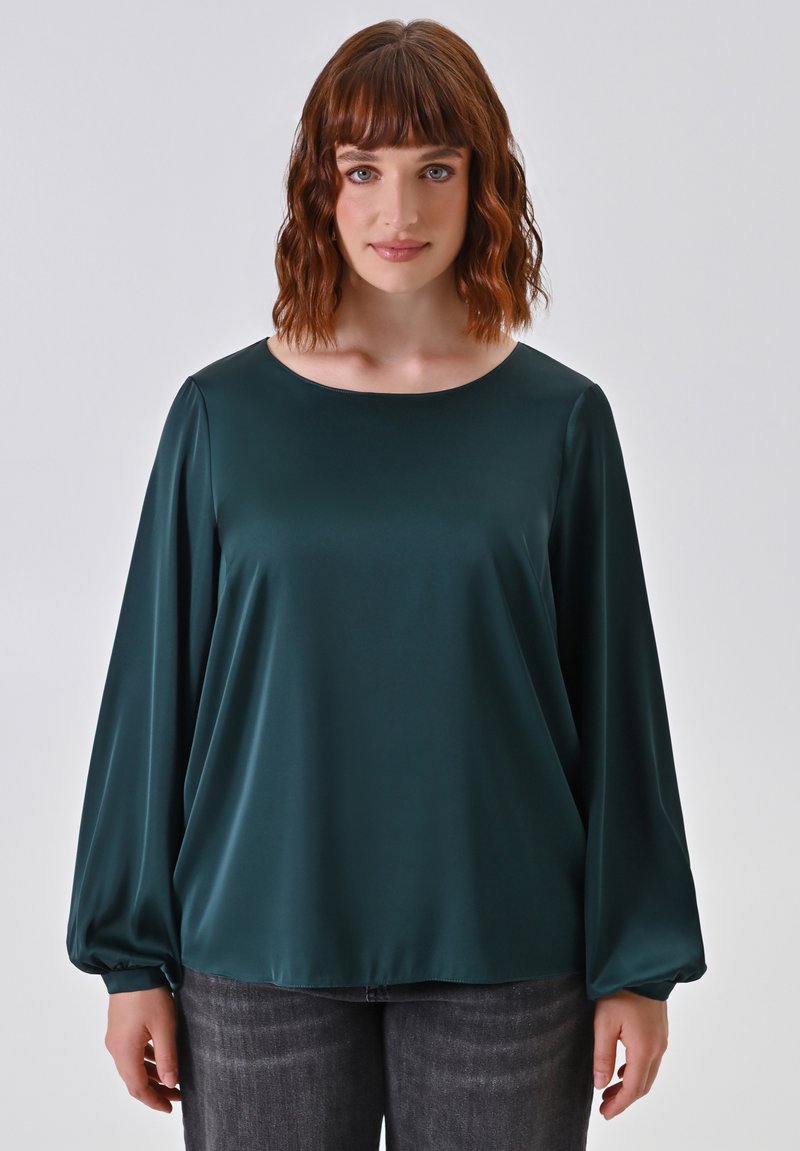Blusa verde scuro a maniche lunghe con una texture liscia e lucida e un ampio scollo rotondo. Vestibilità rilassata con polsini arricciati sui polsi.