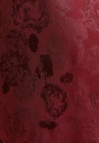 Tkanina w kolorze wina z wypukłym, kwiatowym wzorem, na którym znajdują się ciemnoróżowe motywy. Gładkie wykończenie z delikatnym połyskiem, co nadaje jej bogatą głębię wizualną.