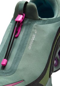 Scarpe Nike Air Max in tessuto verde chiaro con dettagli neri e viola. Presentano un design slip-on e un sistema di allacciatura elastico con una chiusura a scatto.