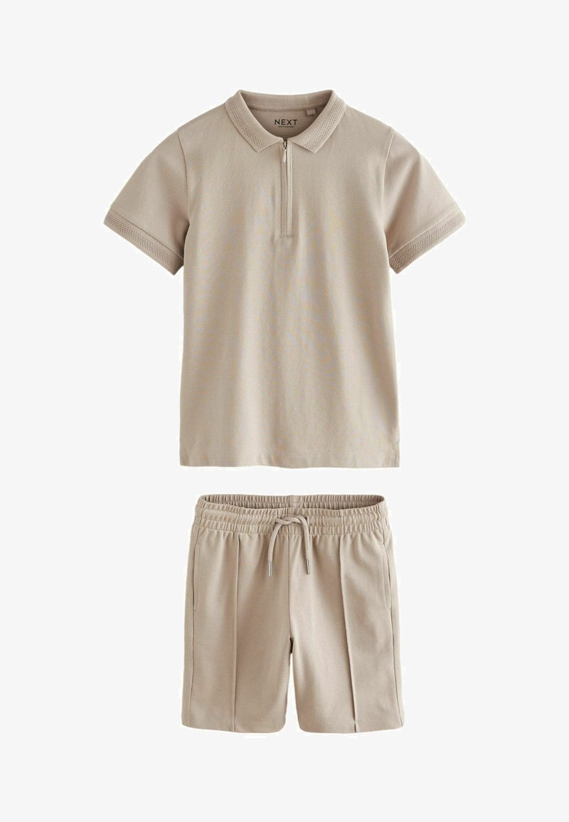 Bež polo majica s kratkim zipom i ovratnikom, uparena s kratkim hlačama koje imaju elastičnu traku i bočne džepove.