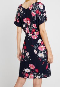 Blumenkleid mit einem marineblauen Hintergrund, das pinke und weiße Blumen zeigt. Kurze Ärmel und eine taillierte Detail, weicher Stoff.