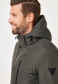 Dark gray jacket with a textured appearance, featuring a hood, front zipper, and side pocket. Includes logo patch on shoulder.