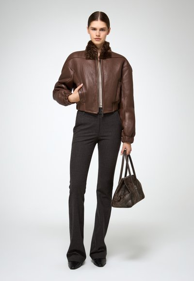 Bruine leren bomberjack met een bontkraag, gecombineerd met donker flared broeken en een gestructureerde handtas in aardetinten.