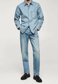 Giacca di jeans azzurro chiaro con una tasca, abbinata a jeans azzurro chiaro coordinati. Entrambi hanno una vestibilità comoda e una texture liscia. Scarpe nere completano il look.