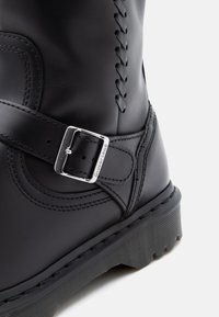 Sorte lærstøvler med sidelukking, sydd detaljer og rillede gummisåler, vist mot en hvit bakgrunn.