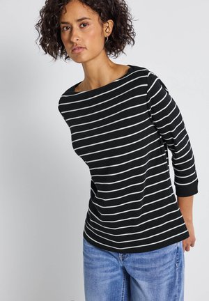 Gestreifte, schwarz-weiße Langarmbluse mit weitem Hals, kombiniert mit hellblauen Jeans, die eine lockere Passform und eine weiche Stoffbeschaffenheit aufweisen.