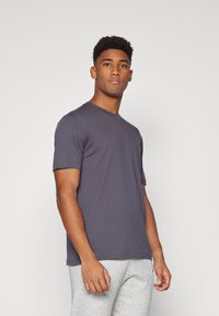 T-shirt gris à manches courtes dans une teinte foncée, en coton doux, avec un col rond et une coupe classique, porté avec un pantalon de survêtement gris.