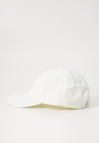 Chapéu de corduroy branco com uma aba ligeiramente curva, topo abotoado e orifícios de ventilação. Apresenta uma pequena etiqueta da marca na parte de trás.