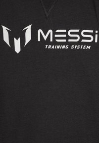 T-shirt in cotone nero con un grande logo bianco "M" e la scritta "MESSi TRAINING SYSTEM", che presenta una superficie liscia e un design a collo a V.