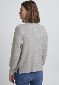 Pull en maille texturée gris clair, à la coupe décontractée, avec des épaules tombantes et des fentes sur les côtés, présentant un ourlet côtelé.