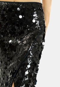 Falda negra de lentejuelas con un diseño ajustado, lentejuelas circulares brillantes y una abertura lateral para mayor detalle y textura.